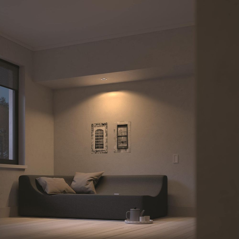 Ein dunkles Sofa mit Kissen steht auf einem Holzboden, daneben eine Teekanne.