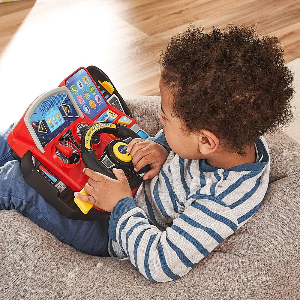 Un jeune enfant joue avec un volant de jeu rouge avec lumières et sons.