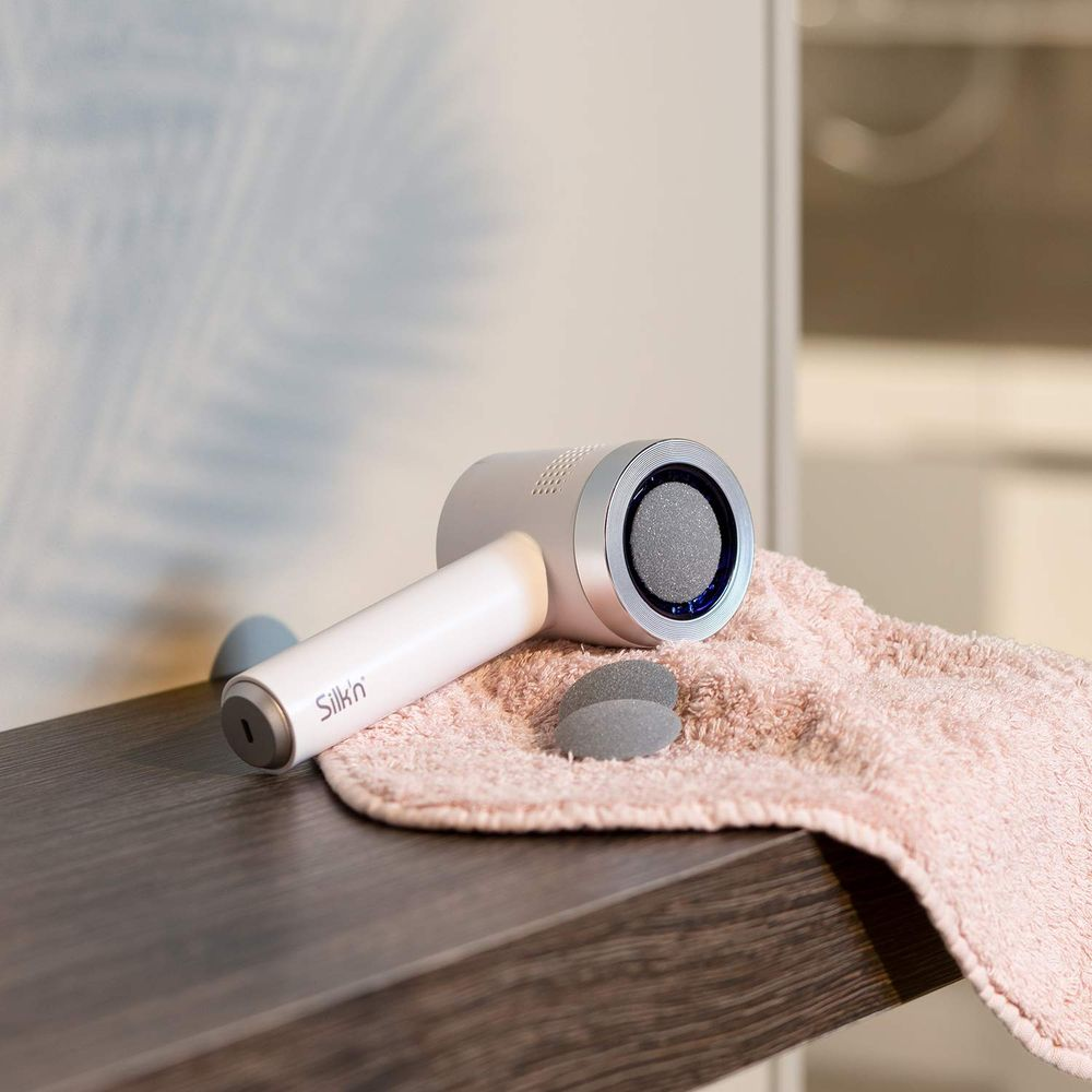 Un esfoliatore elettrico per calli bianco con logo Silkn su un asciugamano rosa.
