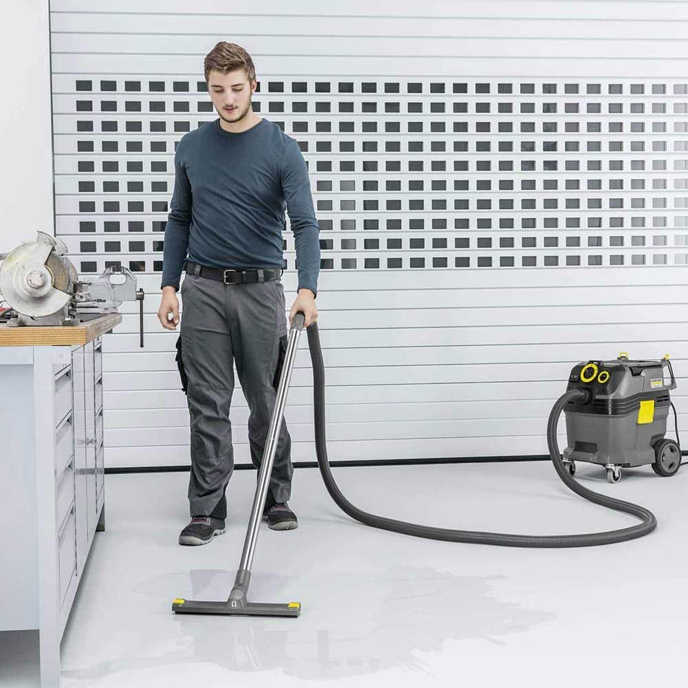 Ein Mann saugt mit einem Industriesauger einen nassen Boden in einer Garage.