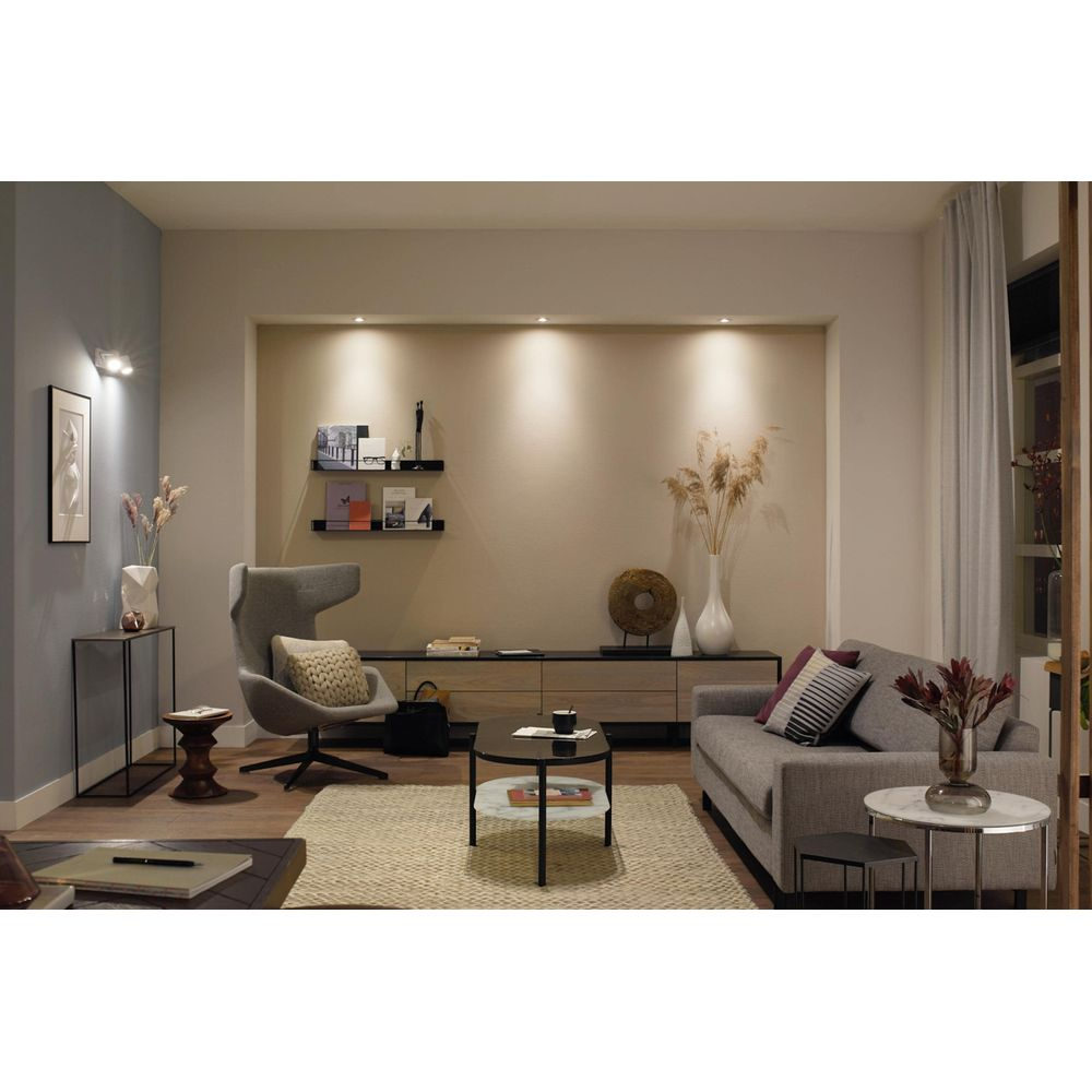 Ein modernes Wohnzimmer mit grauem Sofa, Sessel, Couchtischen und Teppich.