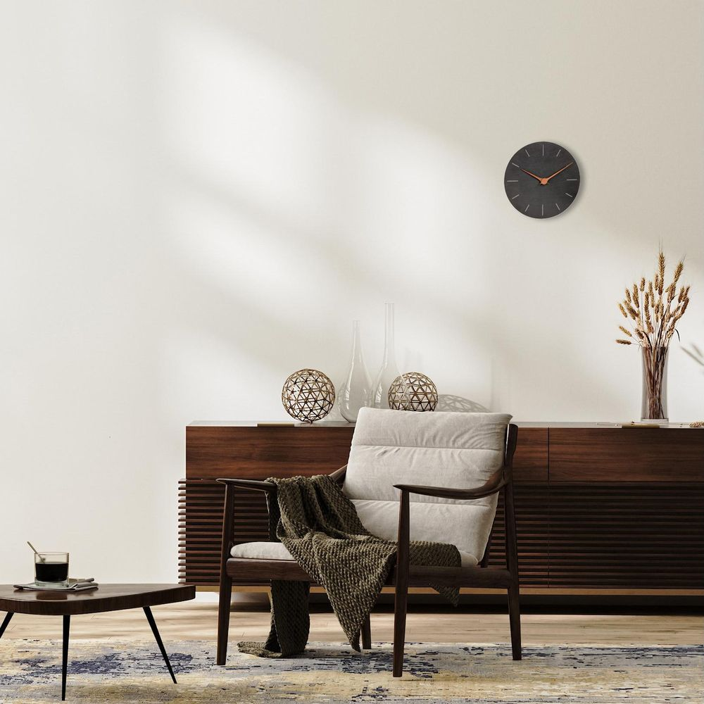 Ein Sessel mit Überwurf steht vor einem dunklen Sideboard. Eine Uhr hängt an der Wand.