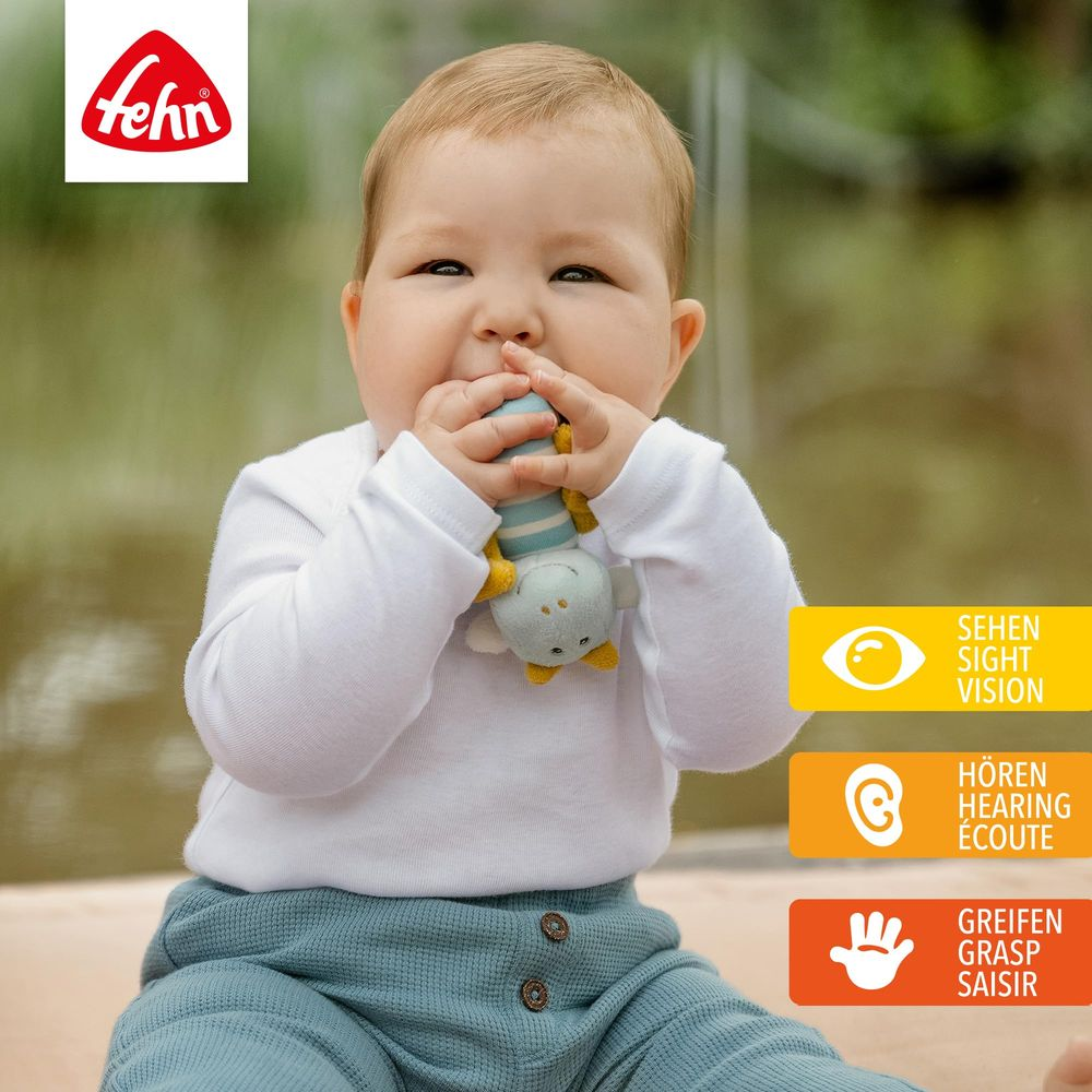 Un bébé mâchouille un jouet. Logo Fehn en haut à gauche.