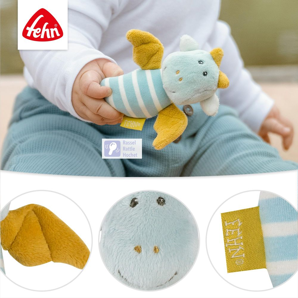 Un bébé tient un jouet dragon en peluche rayé bleu et blanc avec des ailes jaunes.