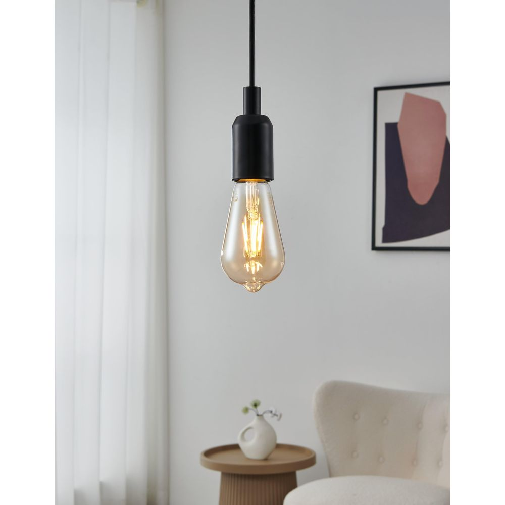 Świecąca żarówka Edison wisi na czarnym kablu nad stolikiem.