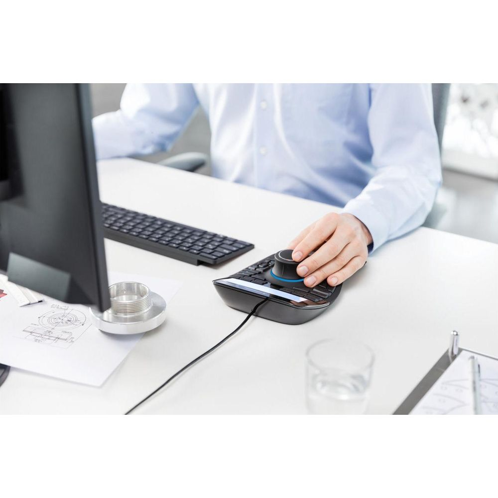 Man in blue shirt uses 3D mouse at desk with computer and blueprints.
