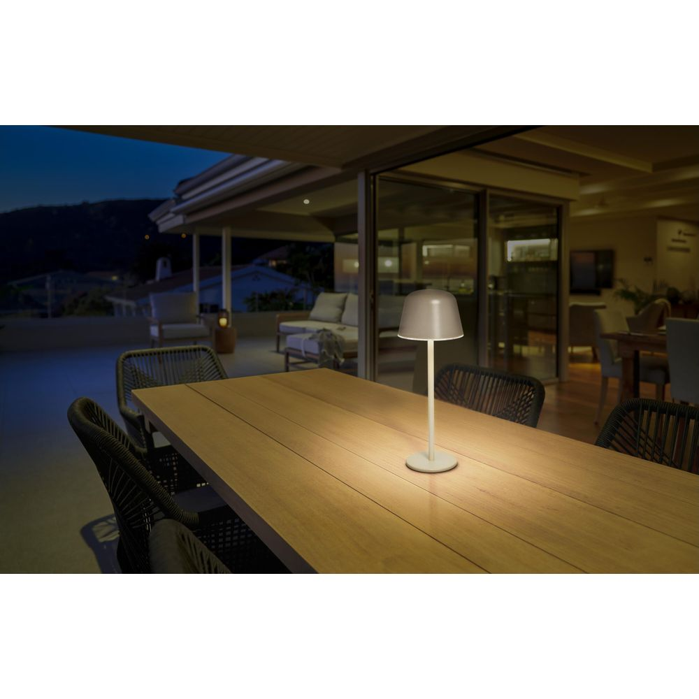 Una lampada da tavolo bianca illumina un tavolo di legno con sedie all'aperto di notte.