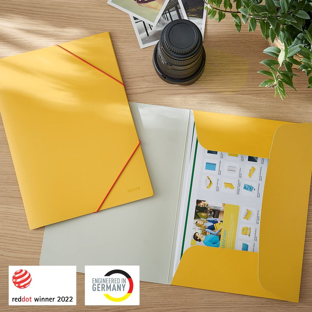 Żółty folder Leitz z czerwonym gumką, otwarty, pokazuje broszurę. Obok obiektyw.