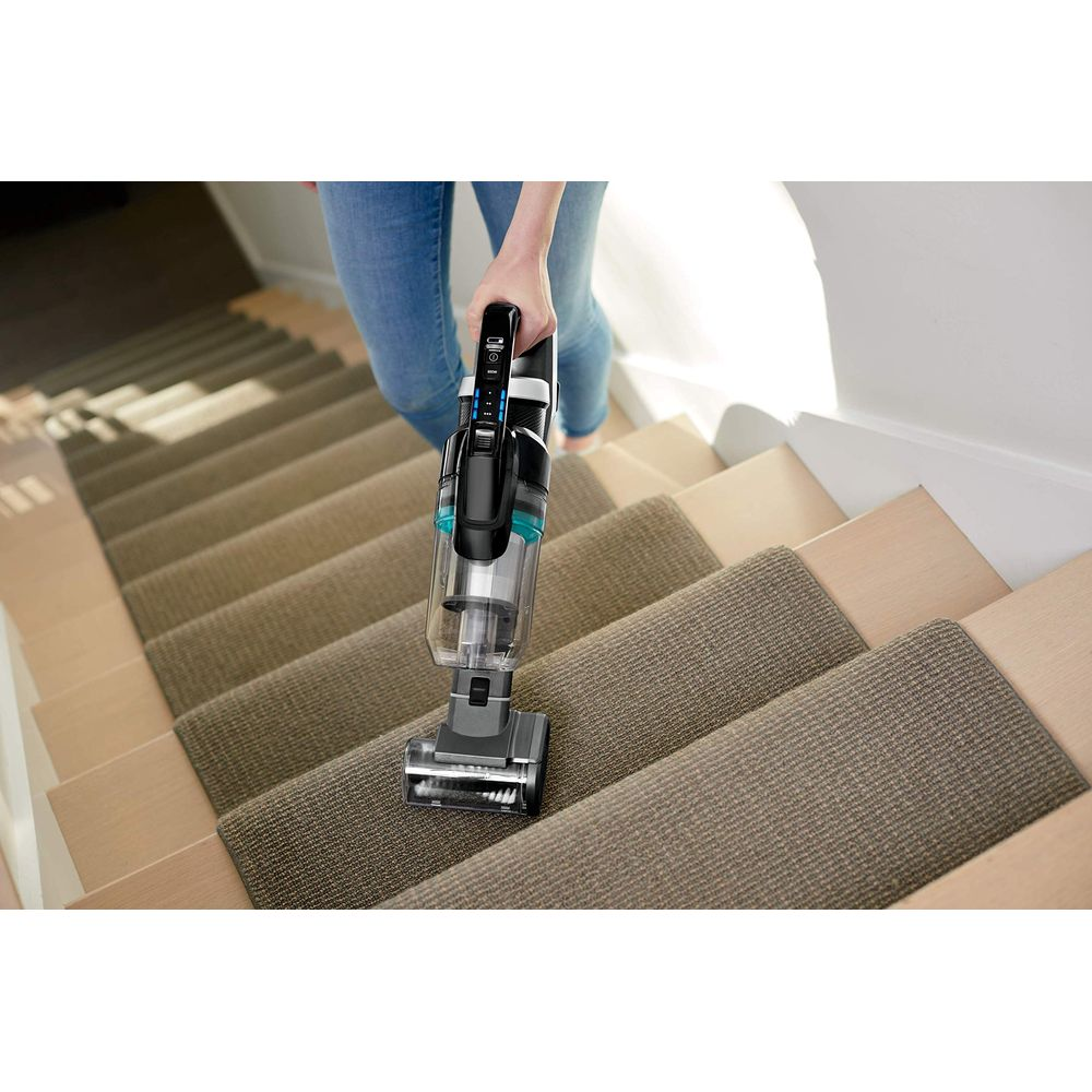 Una persona aspira una scala rivestita di moquette con un aspirapolvere cordless.