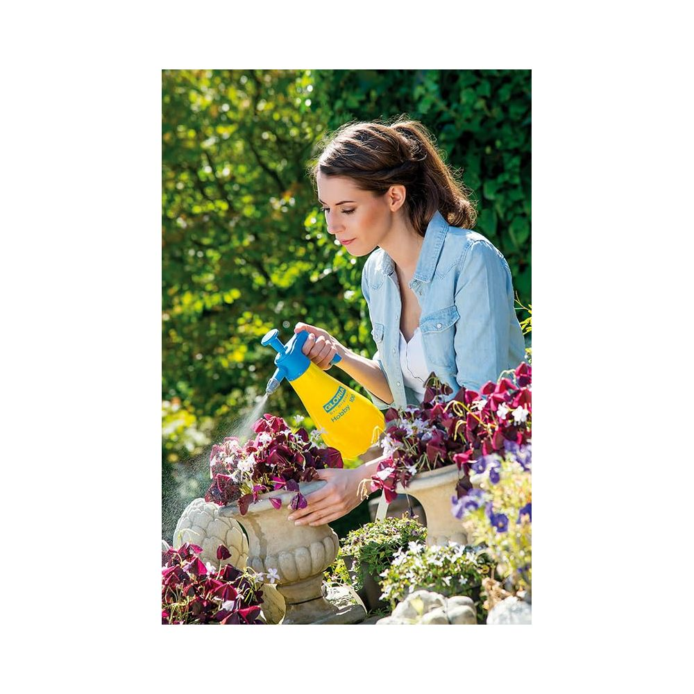 Kobieta w dżinsowej koszuli spryskuje kwiaty w doniczce żółtym opryskiwaczem.