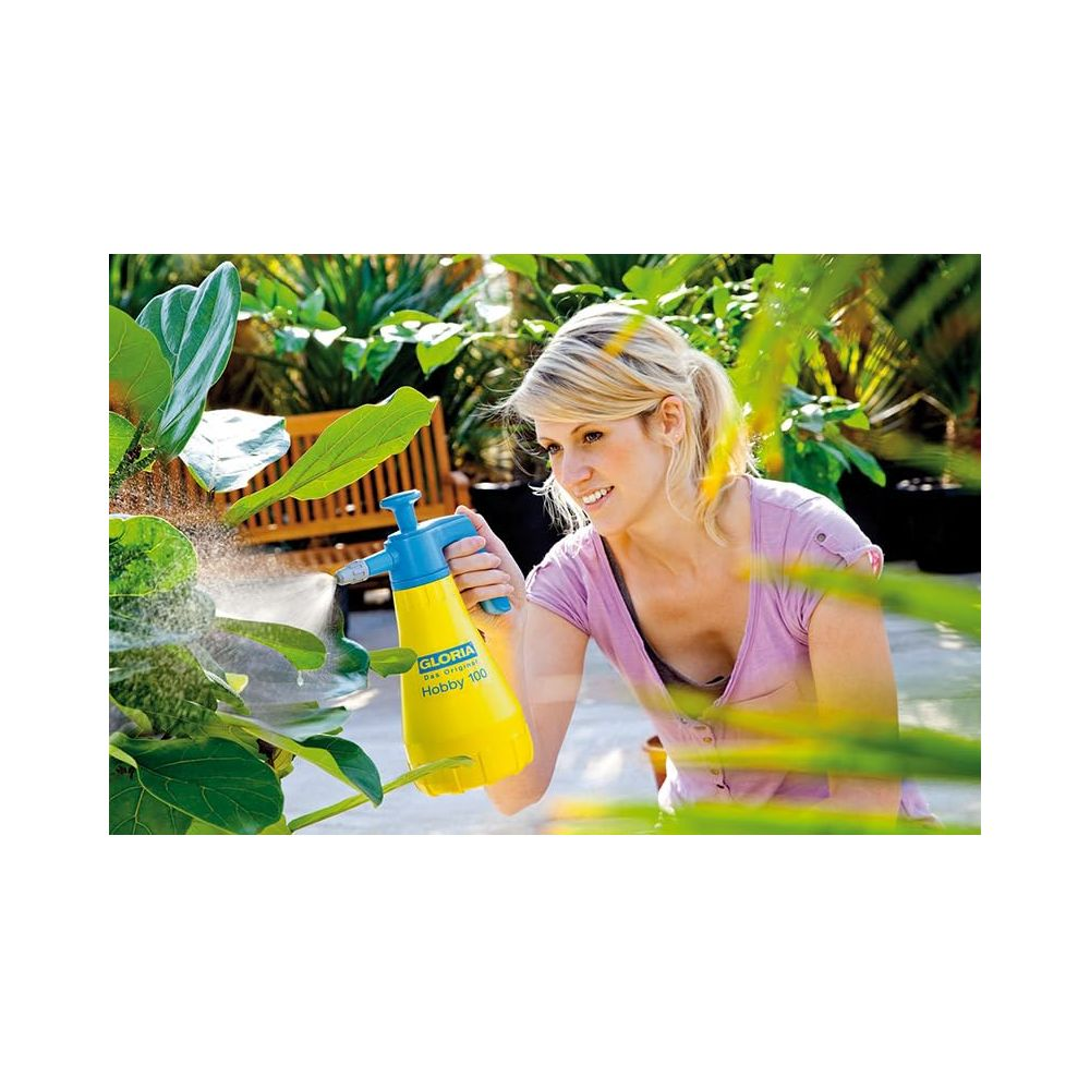 Kobieta spryskuje roślinę żółtym opryskiwaczem w ogrodzie.