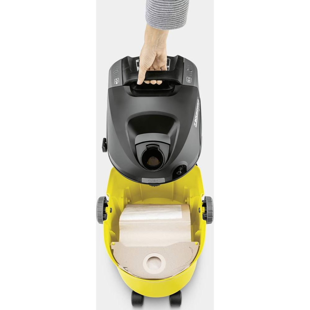 Dłoń podnosi czarny uchwyt odkurzacza. Pojemnik jest żółty.