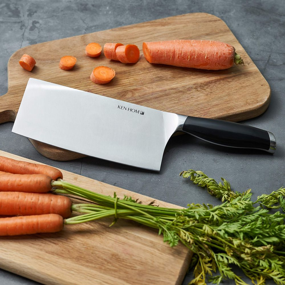 Un couteau de chef repose à côté de carottes entières et coupées sur une planche à découper.