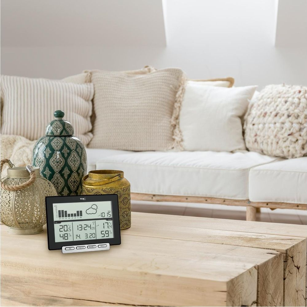 Wetterstation auf einem Holztisch vor einem Sofa mit Kissen.
