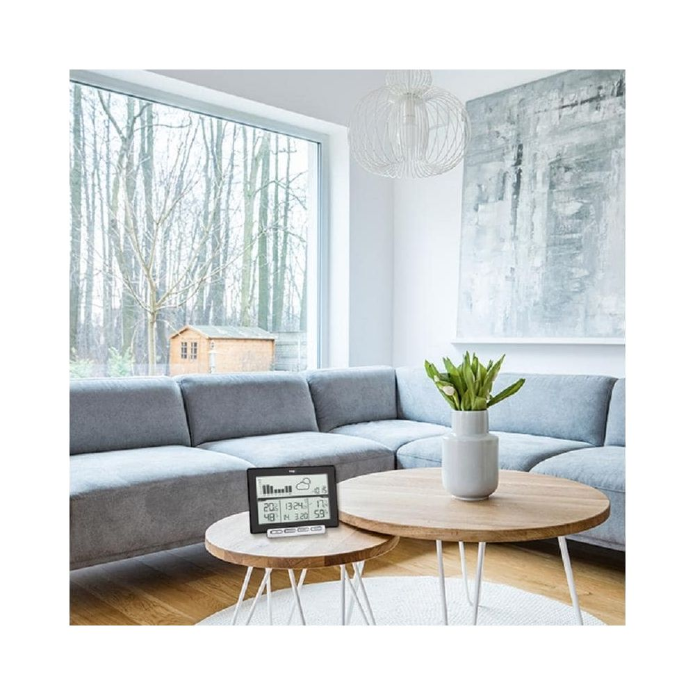 Ein Wohnzimmer mit einem grauen Ecksofa, zwei Holztischen und einem digitalen Wetterdisplay.