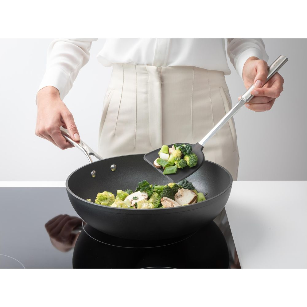 Persona che salta verdure in un wok su piano cottura a induzione.