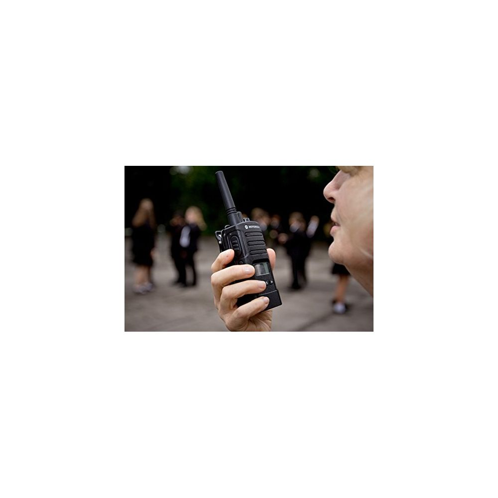 Eine Hand hält ein schwarzes Funkgerät, im Hintergrund eine Gruppe von Personen.