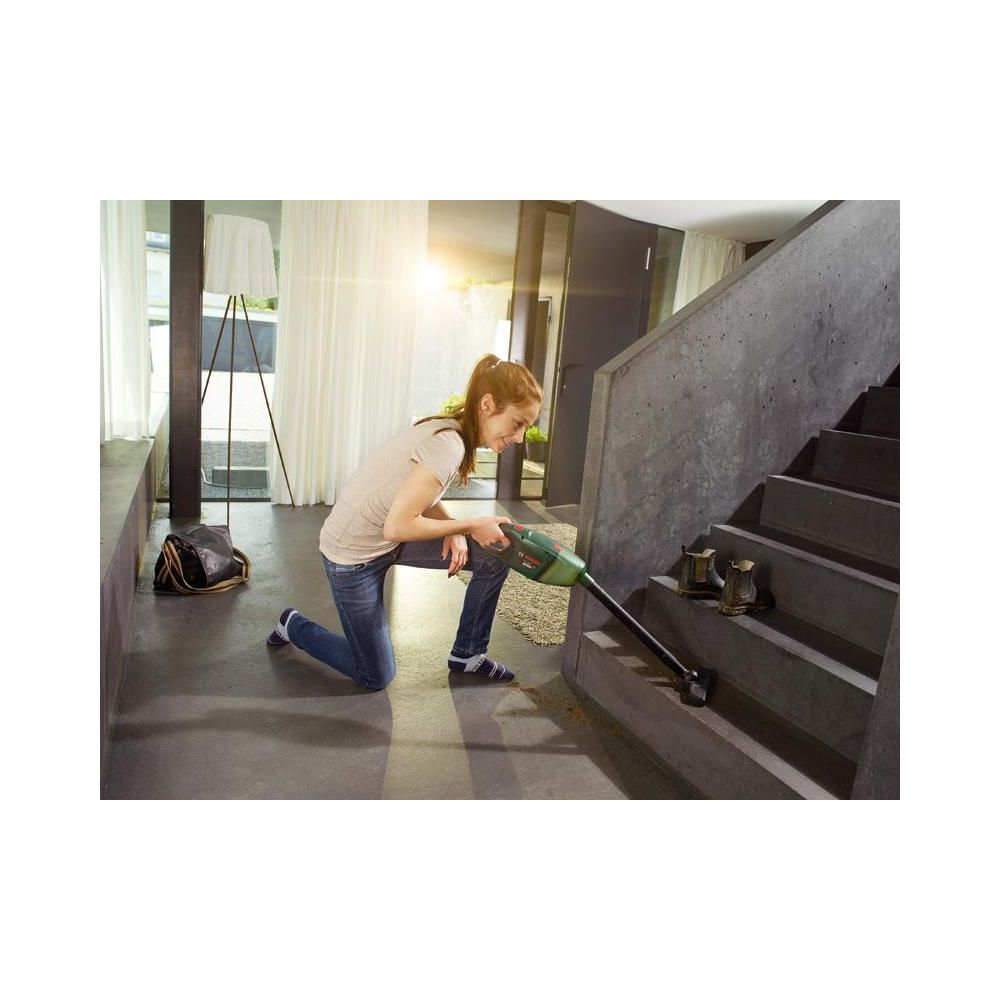 Una mujer aspira una escalera de hormigón con una aspiradora verde.