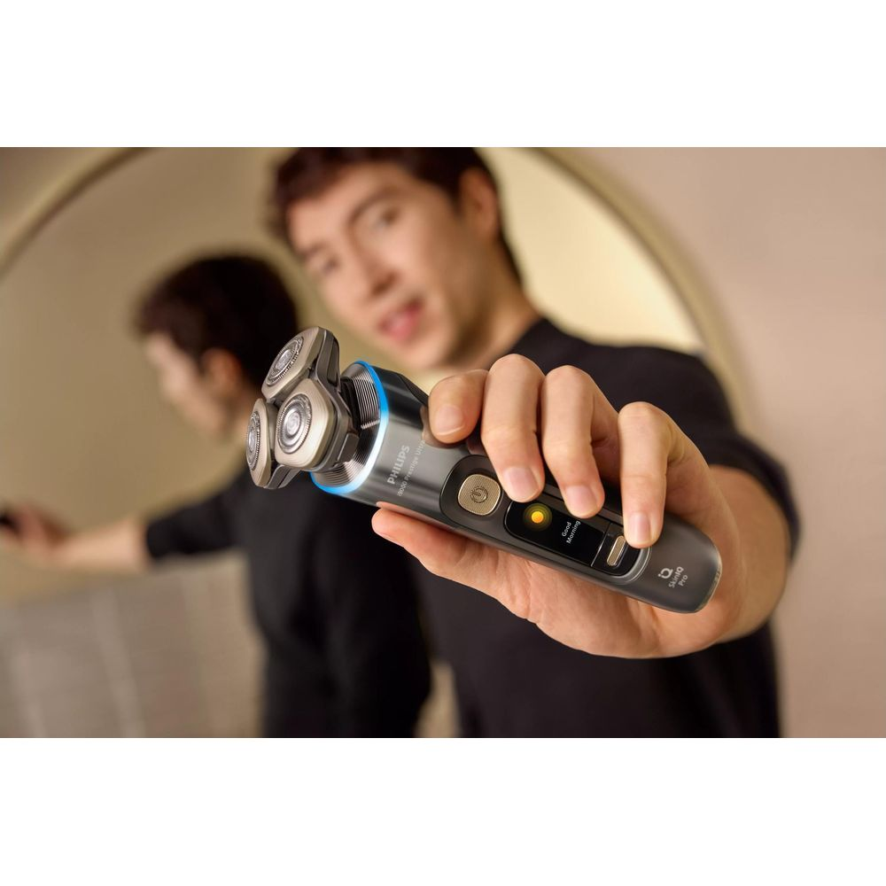 Mężczyzna trzyma elektryczną golarkę Philips z trzema obrotowymi głowicami i cyfrowym wyświetlaczem.