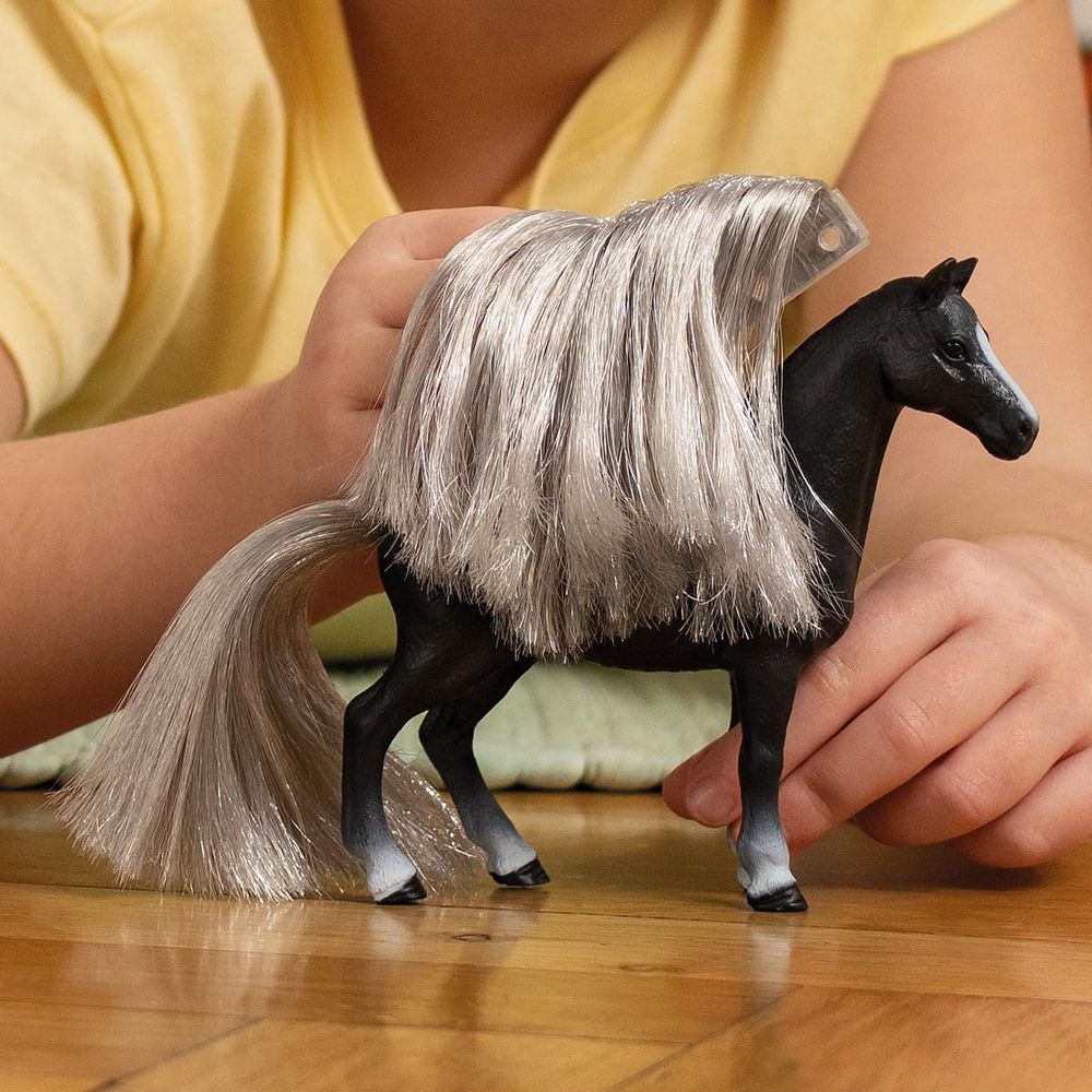Cavallo giocattolo nero con lunga criniera grigia, tenuto da mani di bambino.