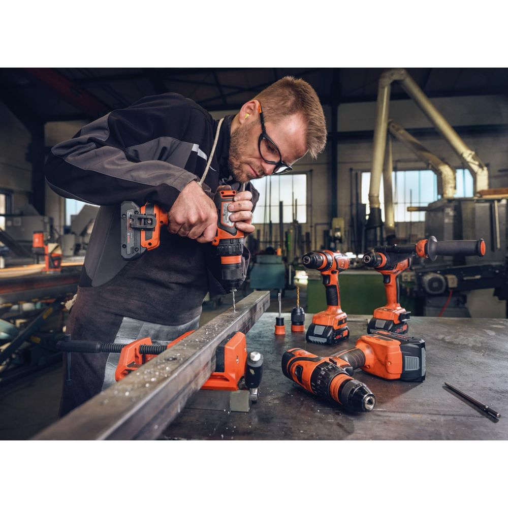Ein Mann bohrt Metall mit einem orangen Akkuschrauber in einer Werkstatt.