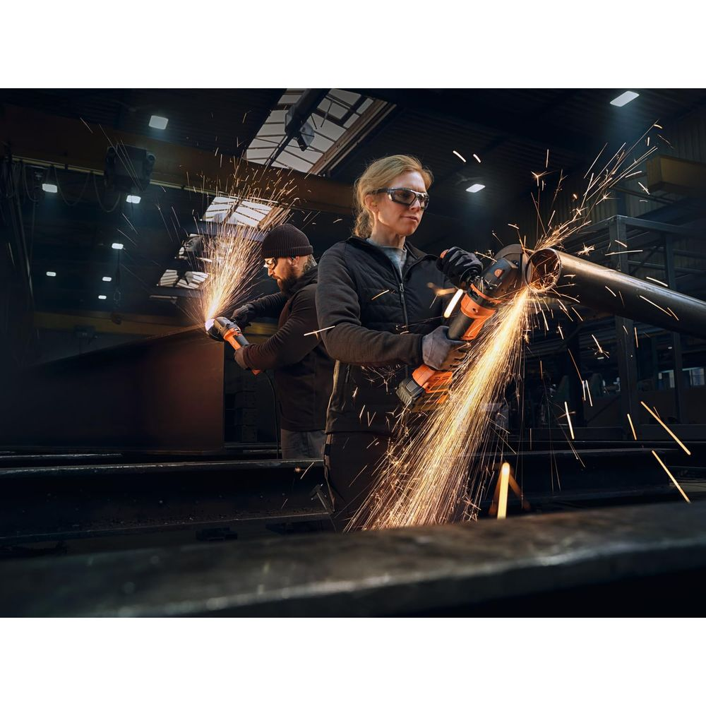 Zwei Arbeiter in einer Fabrik benutzen Winkelschleifer und erzeugen helle Funken. Einer schneidet Rohr, der andere Metall.