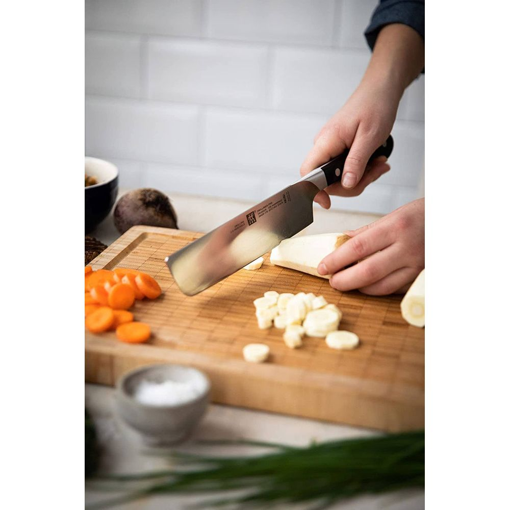 Ręce kroją czosnek i warzywa korzeniowe na drewnianej desce nożem.