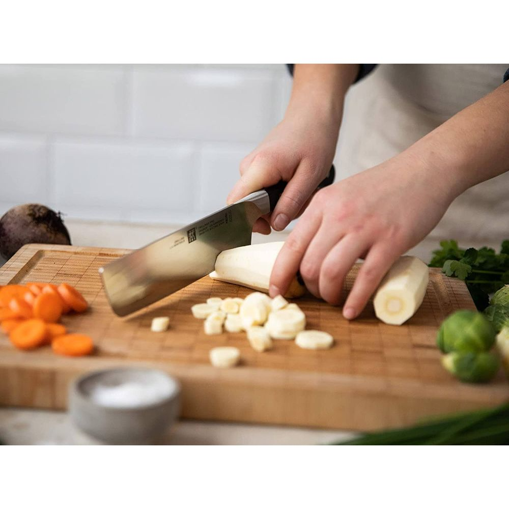 Ręce krojące pasternak na desce drewnianej z marchewkami, burakiem i solą.