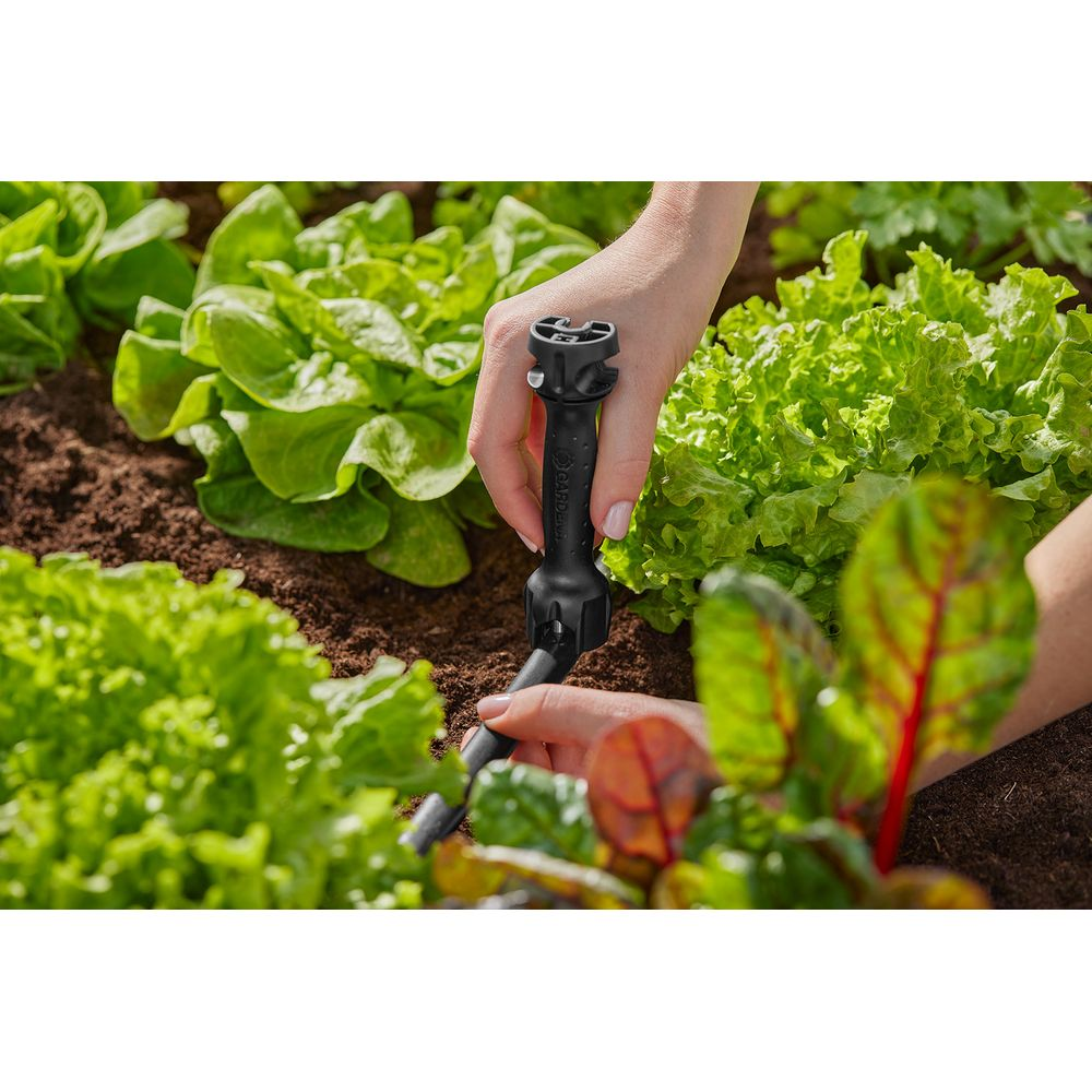 Handen installeren een zwart irrigatieventiel in een moestuin.