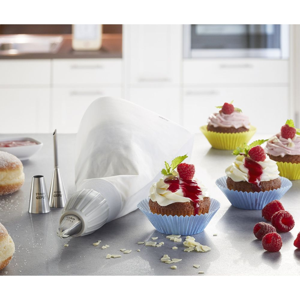 Ein Spritzbeutel mit Aufsätzen und Cupcakes mit Himbeeren und Zuckerguss.
