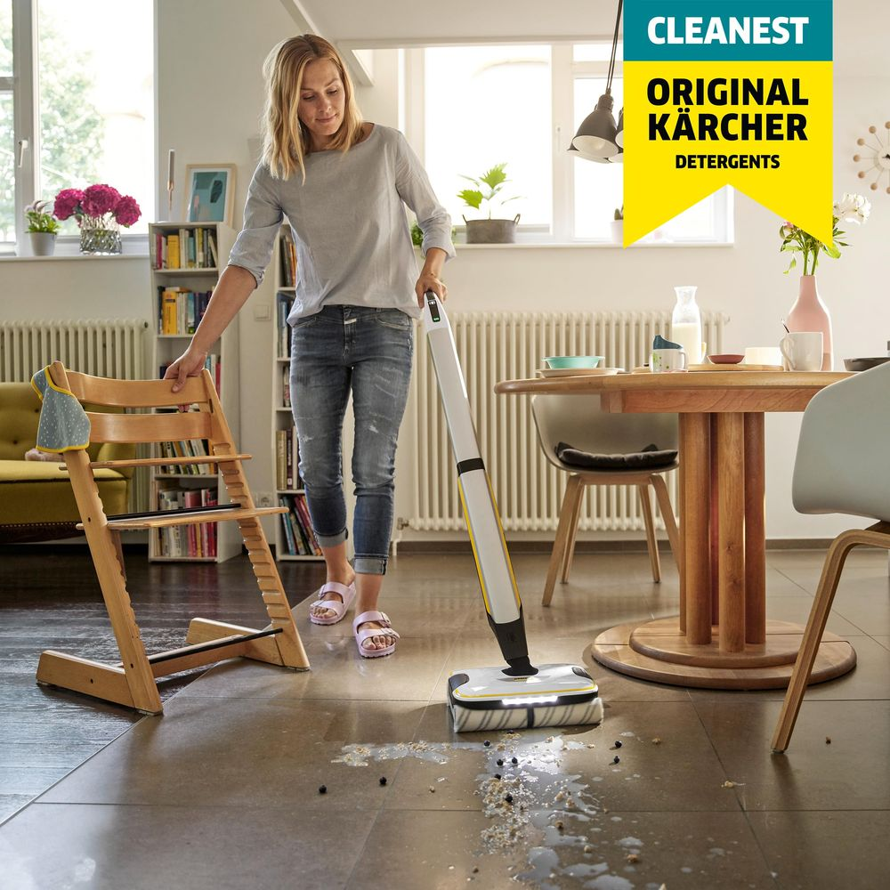 Donna pulisce pavimento con Kärcher. Seggiolone per bambini vicino.