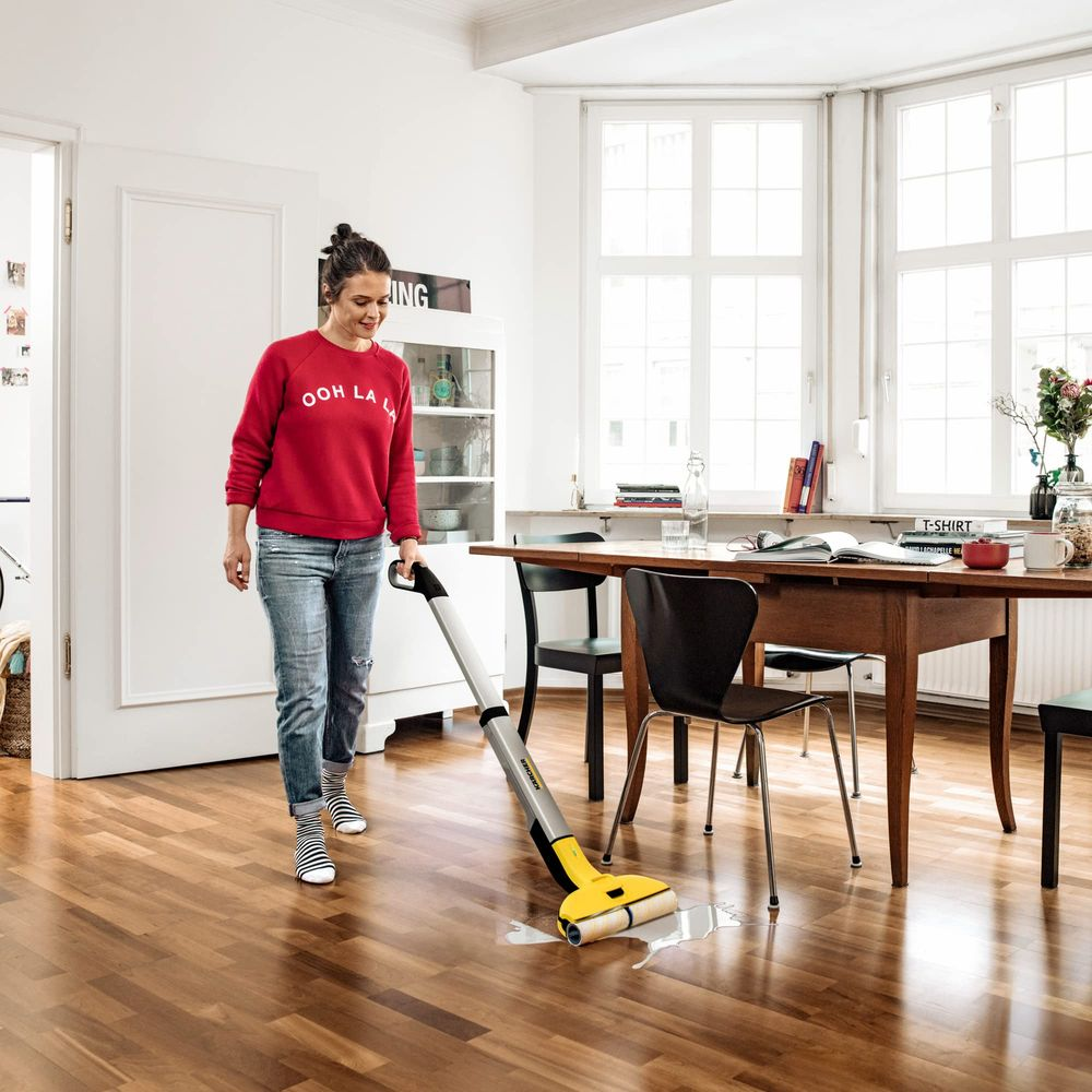Donna pulisce pavimento in legno con aspirapolvere bagnato giallo che raccoglie acqua.