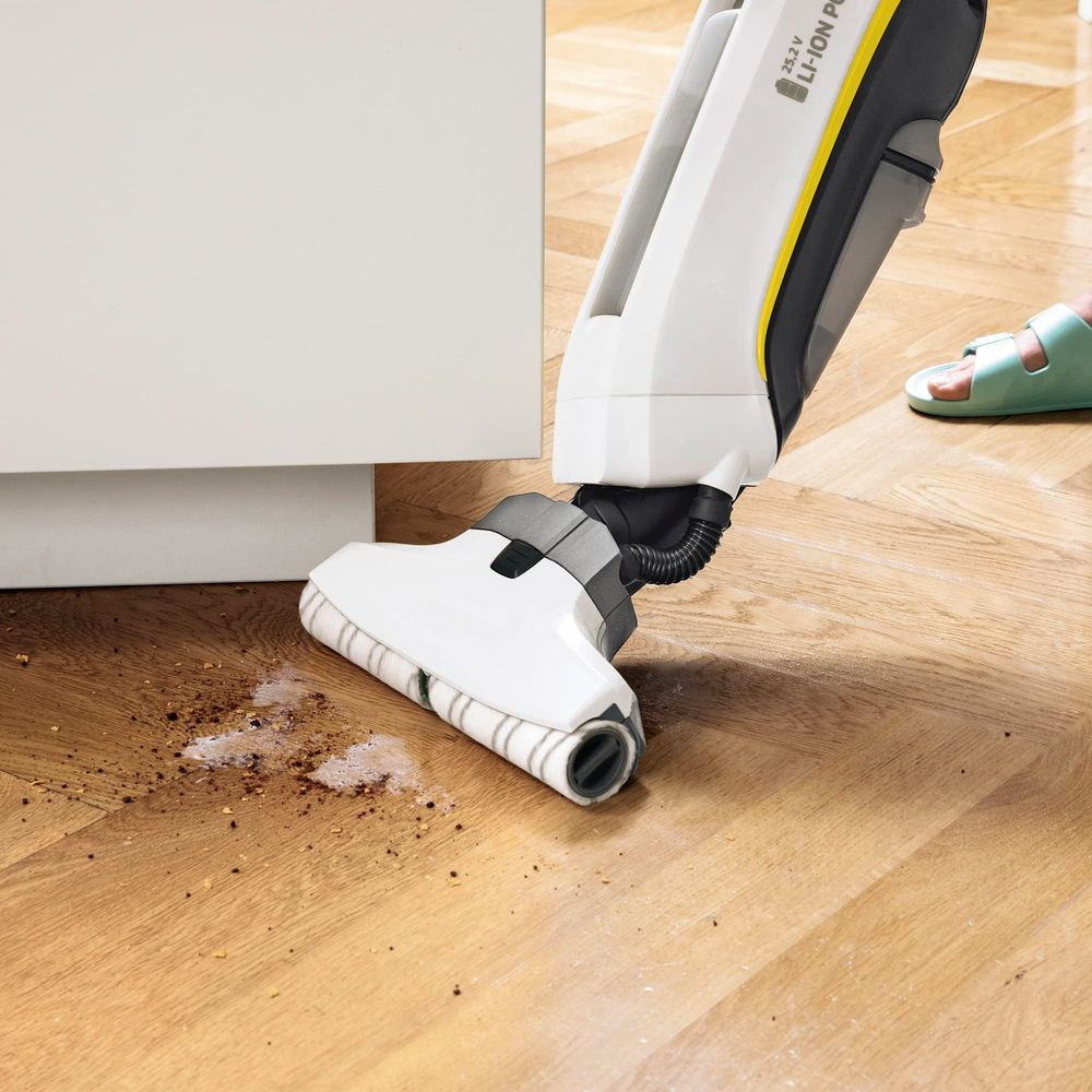 Un aspirapolvere senza fili pulisce un pavimento in legno con sporco e umidità.