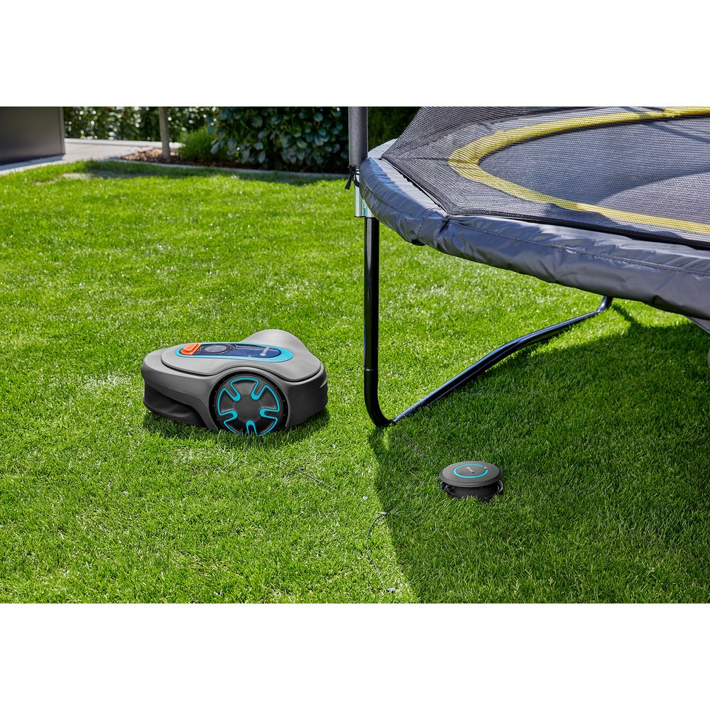Un robot tosaerba e una stazione di ricarica su erba verde accanto a un trampolino.