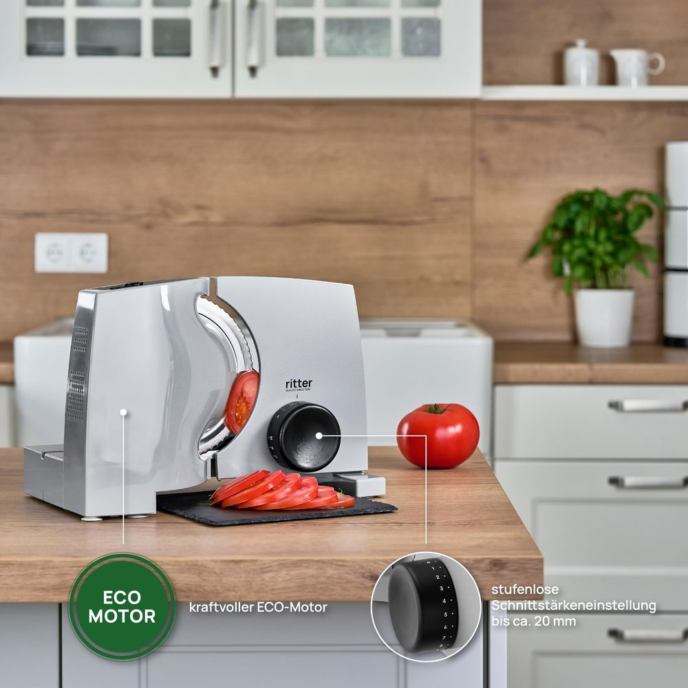 Srebrna krajalnica kroi pomidora na drewnianym stole. Obok leżą plasterki pomidora.