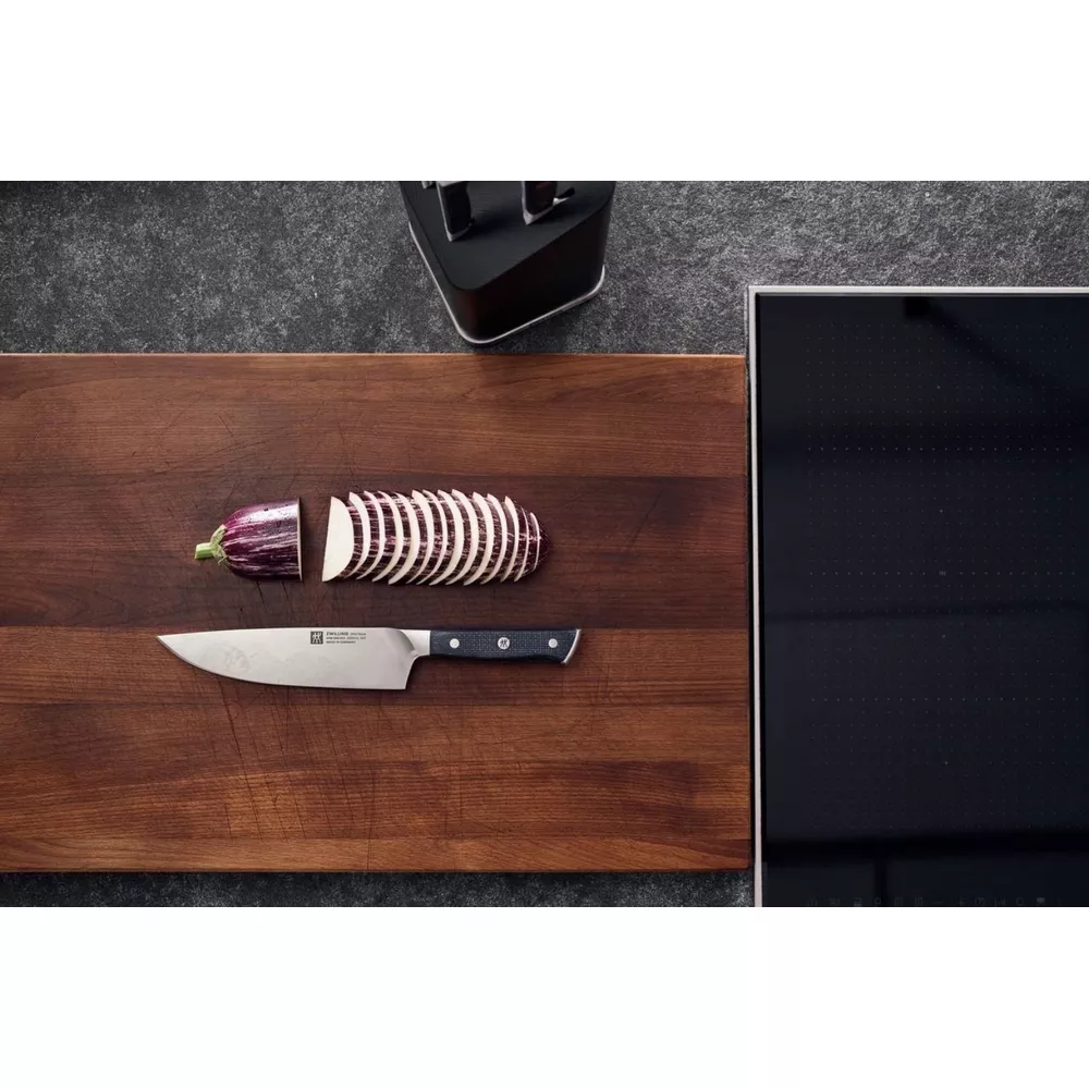 Pokrojony bakłażan i nóż na drewnianej desce obok płyty grzewczej.