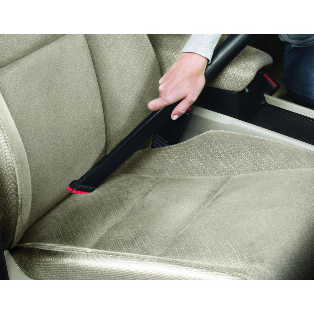 Una mano usa un aspirapolvere nero per pulire un sedile dell'auto beige.