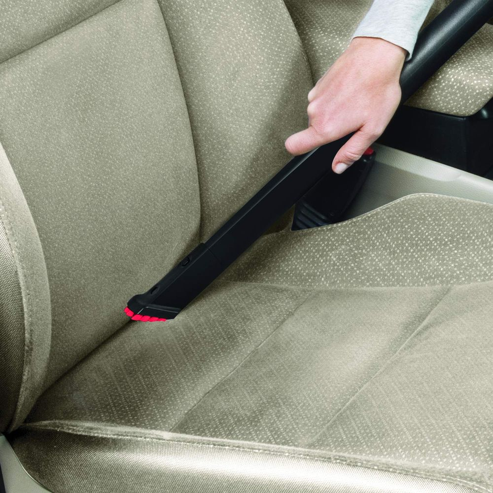 Una mano usa un aspirapolvere per pulire un sedile dell'auto beige.