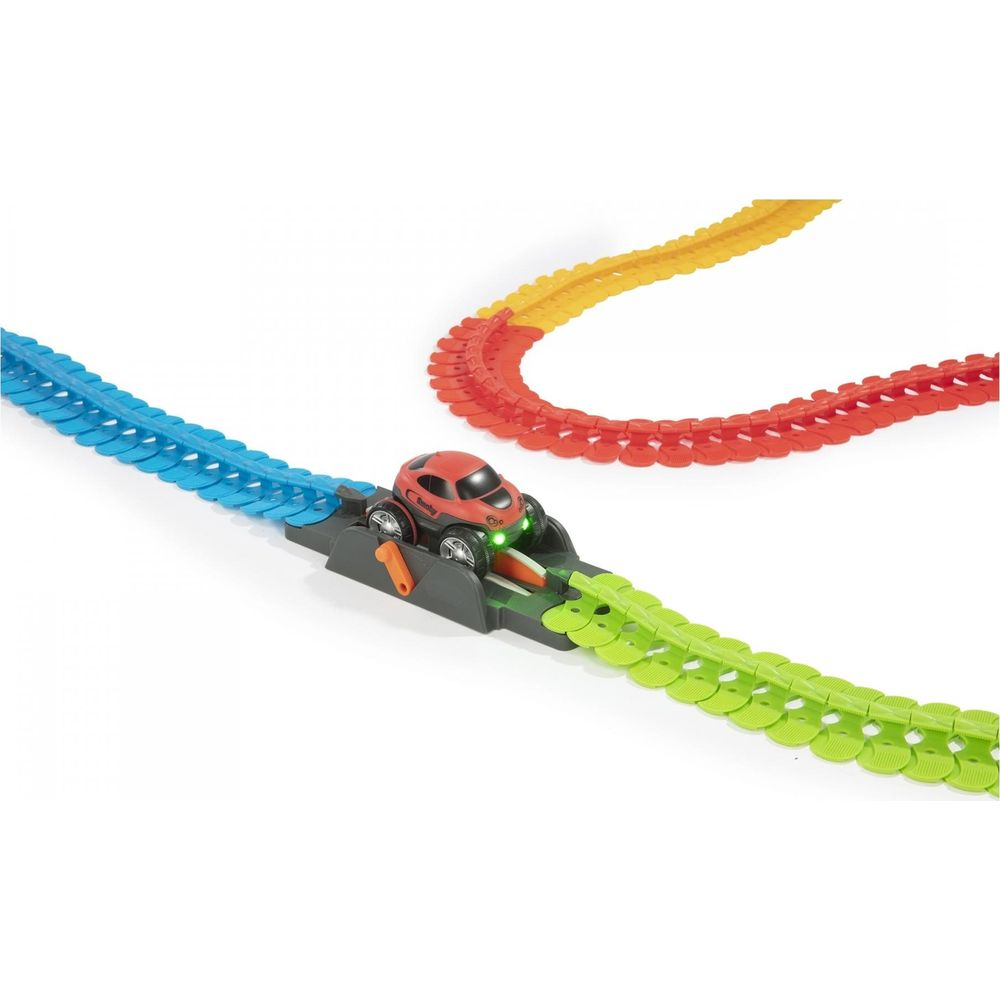 Czerwony samochodzik stoi na szarej podstawie połączonej z zielonymi torami. W pobliżu niebieskie i czerwono-żółte tory.