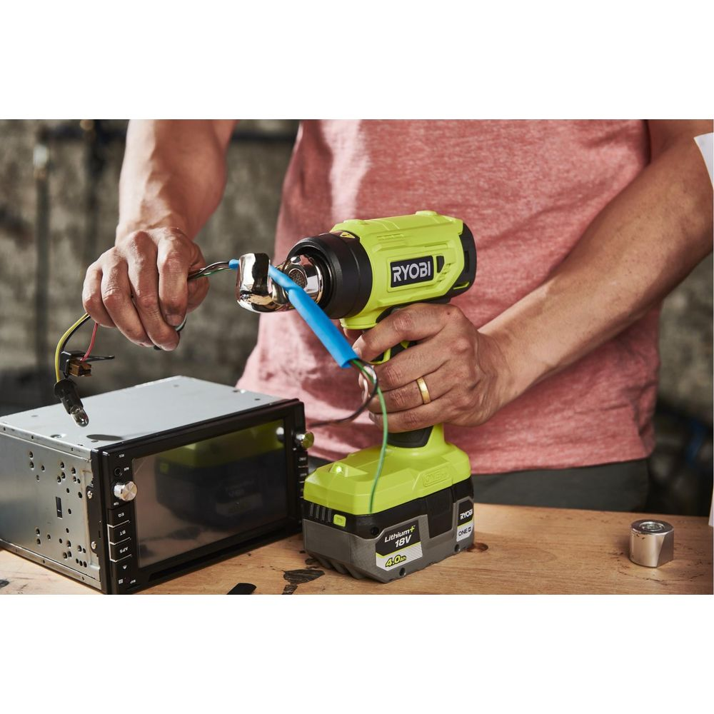Une personne utilise un pistolet à air chaud Ryobi pour connecter des fils à un autoradio.