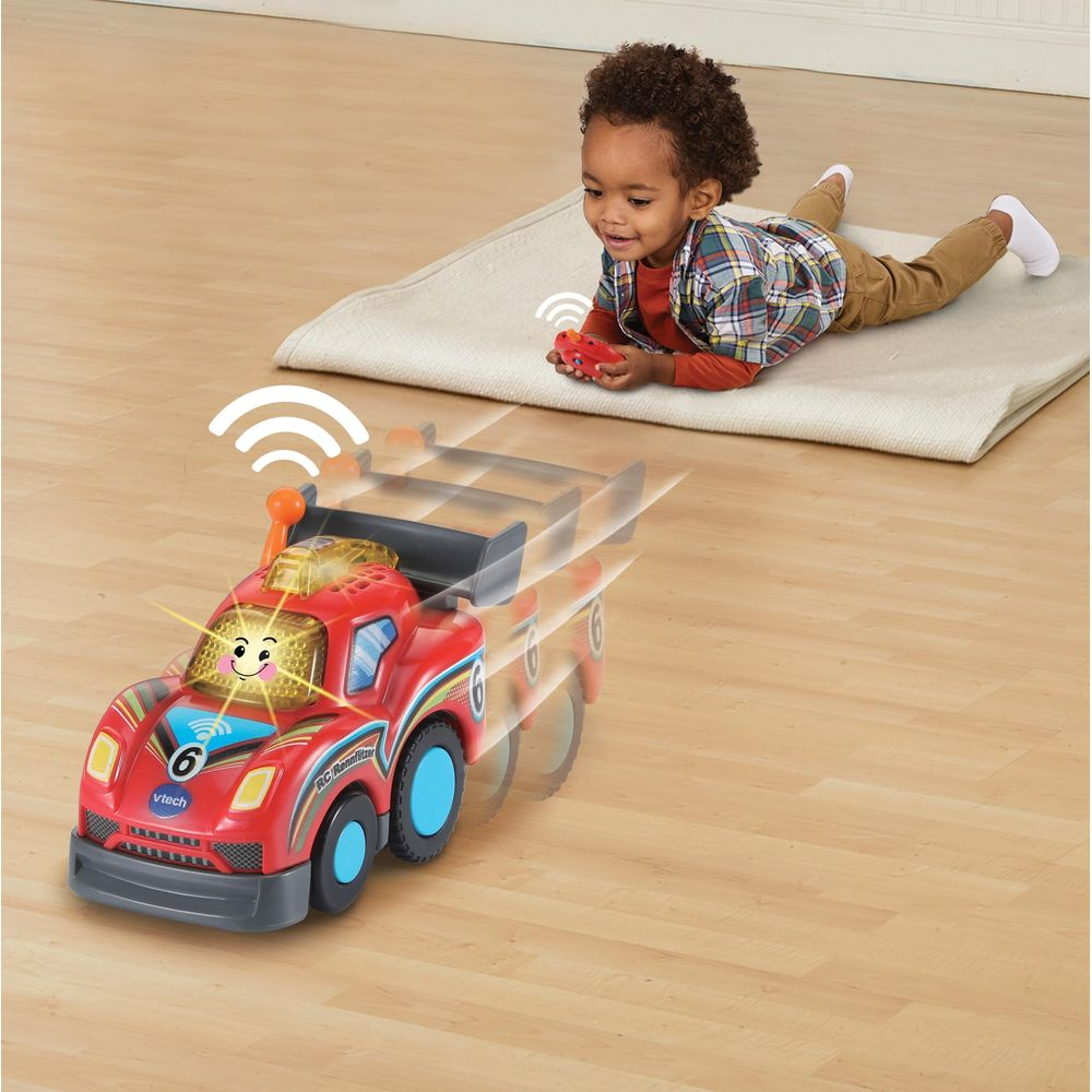 Ein Kleinkind spielt mit einem roten RC-Rennwagen auf einem Teppich und steuert ihn mit einer Fernbedienung.
