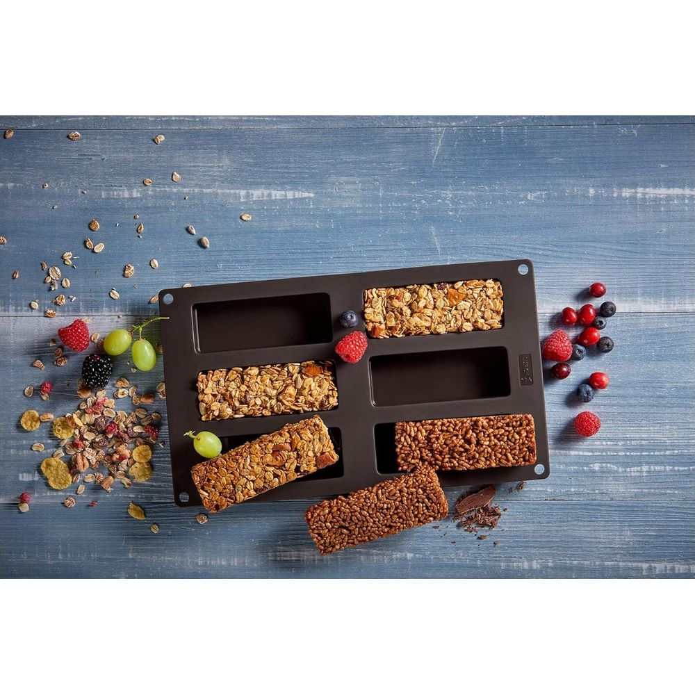 Batony czekoladowe i musli w ciemnej formie na drewnianym tle.