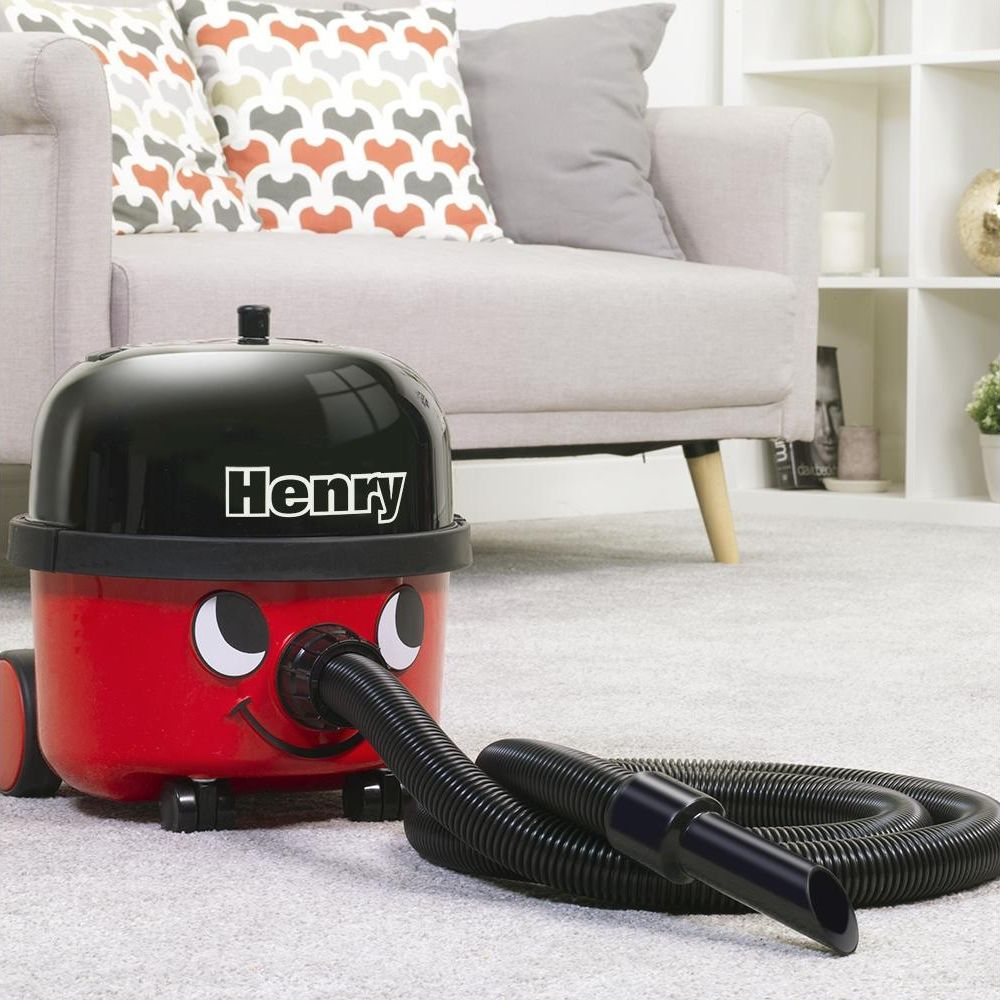 Un aspirapolvere rosso Henry con parte superiore e tubo neri siede su un tappeto.