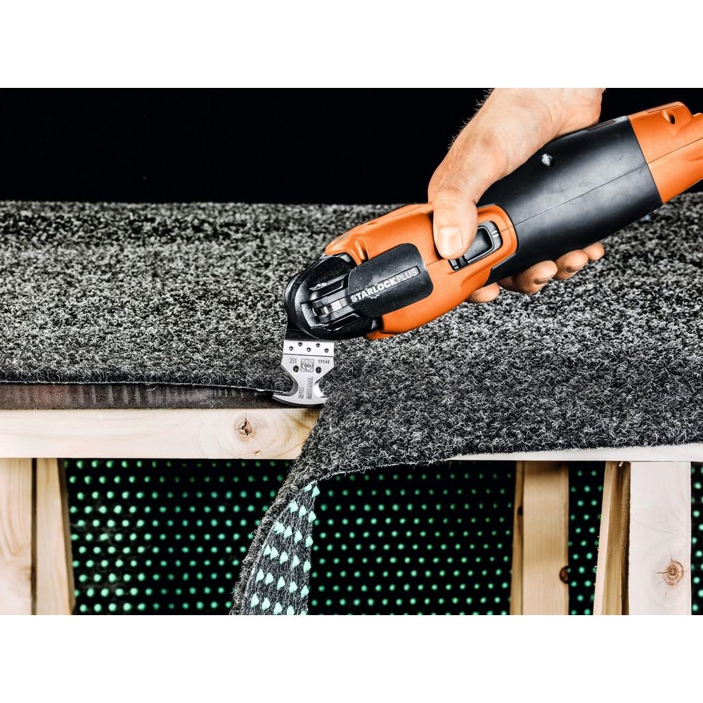 Ein Mann schneidet mit einem orangefarbenen Werkzeug grauen Teppich auf einer Holzkonstruktion.