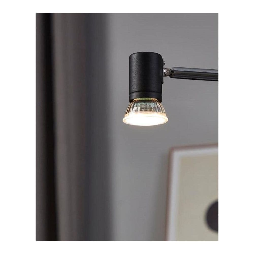 Une tête de lampe noire avec détail de verre est éclairée, avec rideau et cadre en arrière-plan.