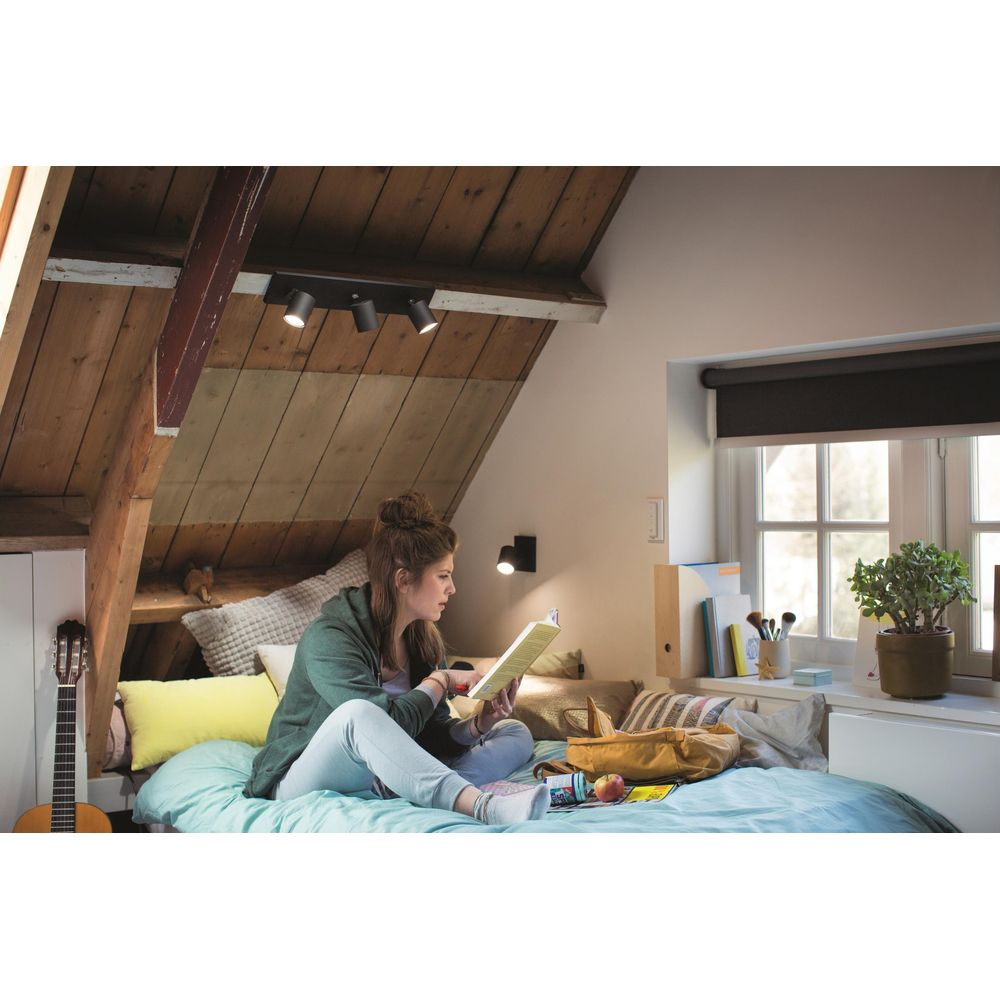 Jeune femme lit sur un lit sous des plafonds mansardés. Guitare et lampe visibles.