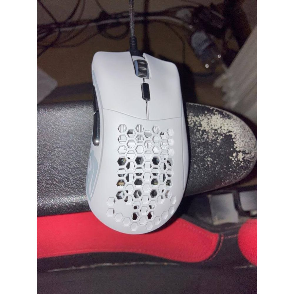 Biała mysz gamingowa z wzorem plastra miodu spoczywa na czerwono-czarnej powierzchni.