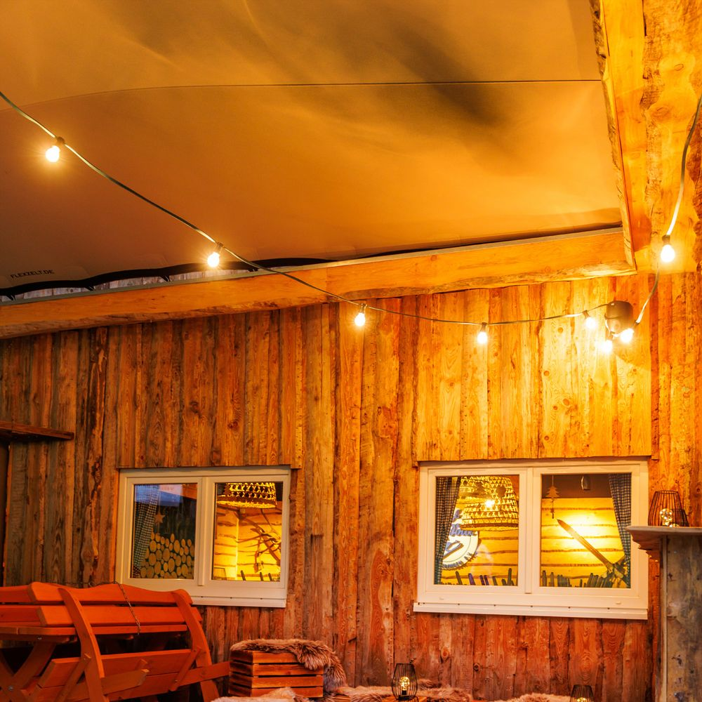 Houten hut met lampjes, bankje en ramen in avondlicht.