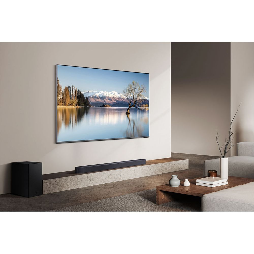 Ein schwarzer Subwoofer und eine Soundbar vor einem großen Fernseher, der eine Berglandschaft zeigt.