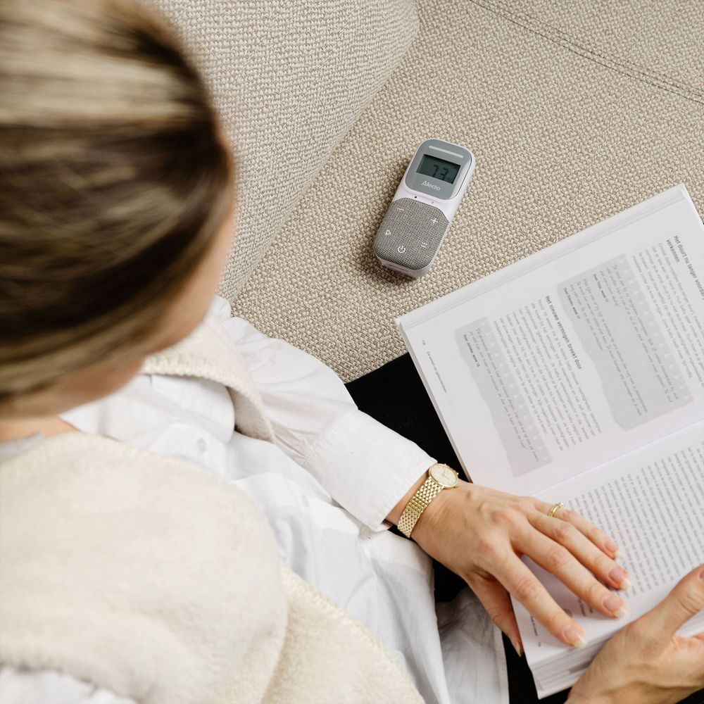 Eine Frau mit einem Buch und einem Babyphone auf einer Couch